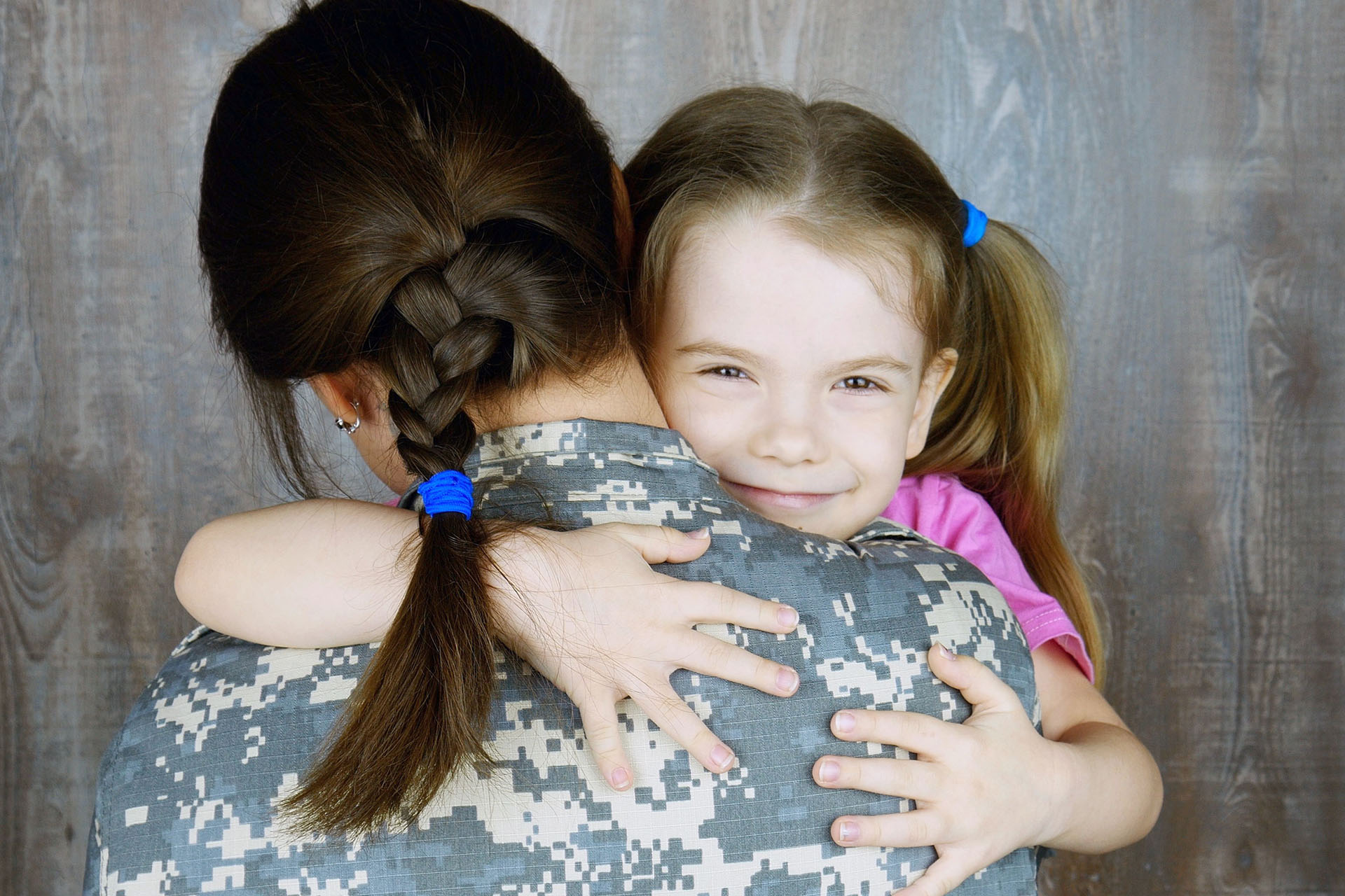 A smiling little girl hugging a female soldier