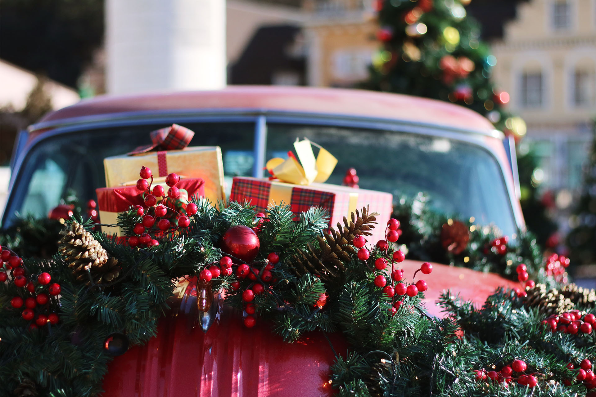 A red car with green holiday garland and wrapped gifts on its hood.